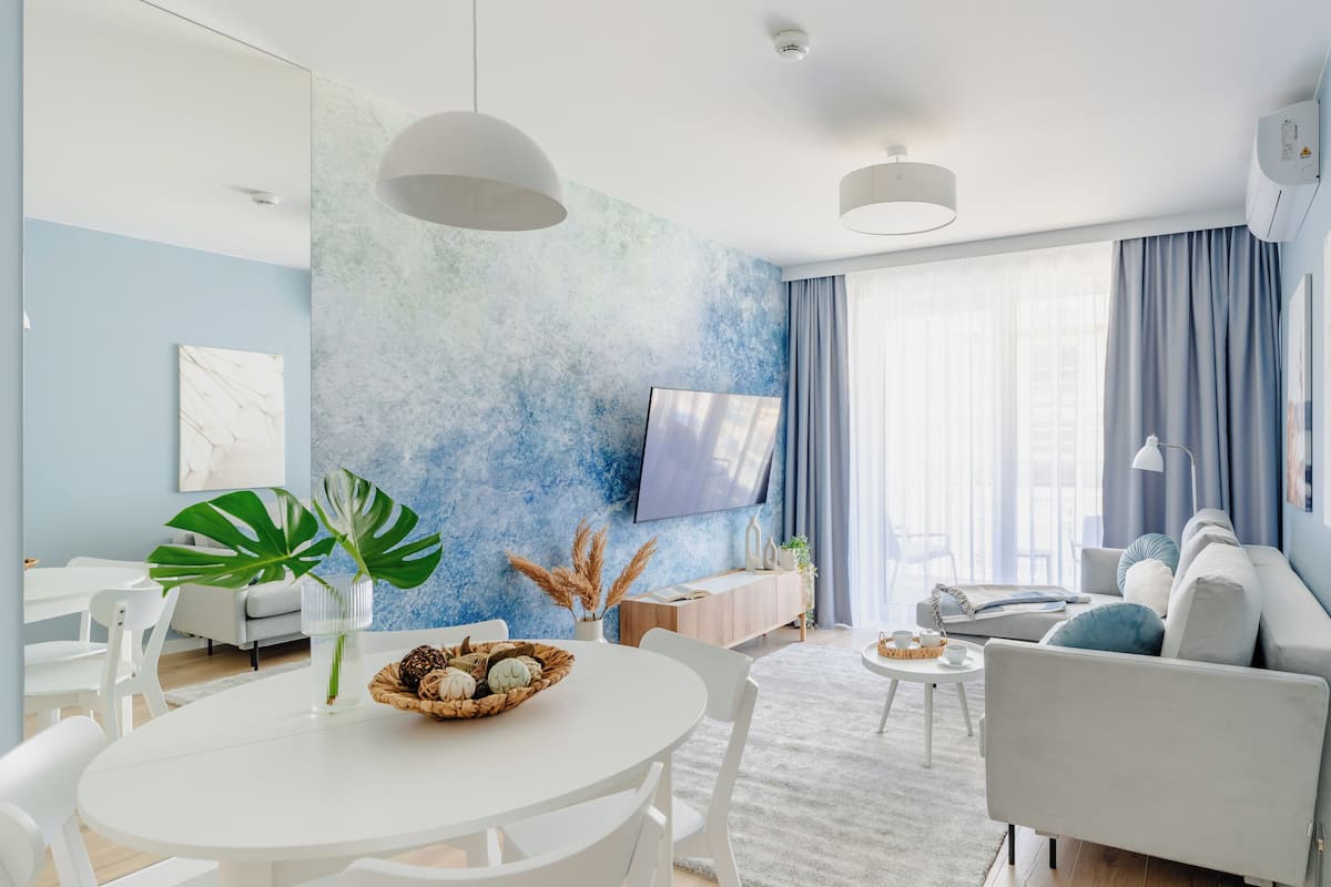 Un salon moderne avec une table à manger ronde, des chaises blanches, un canapé et un téléviseur fixé au mur.