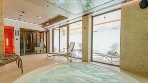 Un espace piscine intérieur moderne, doté d’un jacuzzi, de sièges et de grandes fenêtres.
