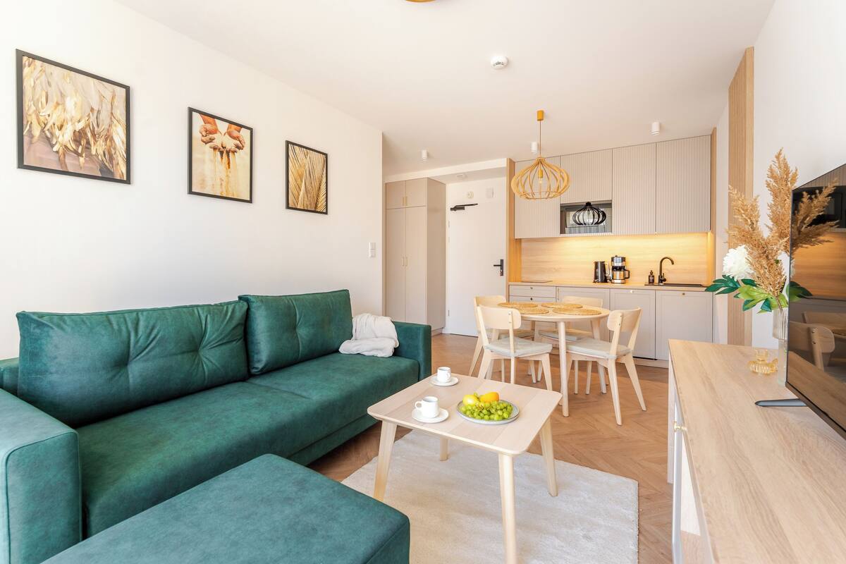 Un salon moderne avec un canapé vert, une table à manger avec des chaises et, au fond, un coin cuisine.