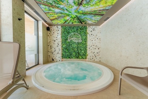 Ein Wellnessbereich mit Whirlpool, einem Sessel und einer Wand mit grüner Bepflanzung.