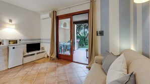 Un espacio habitable compacto con kitchenette, un sofá y puerta corrediza de vidrio que da a un área exterior.