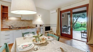 Comedor con una mesa dispuesta para cuatro, cocina al fondo y puerta corrediza de vidrio que da a un área exterior.