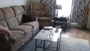 Ein Wohnzimmer mit einer Couch, einem Couchtisch, einem Sessel und einem Vorhang mit Giraffenmuster.