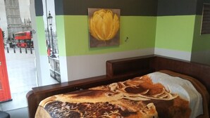 Ein Zimmer mit einem Bett, einem Blumenbild an der Wand und Blick auf einen roten, zweistöckigen Bus draußen.