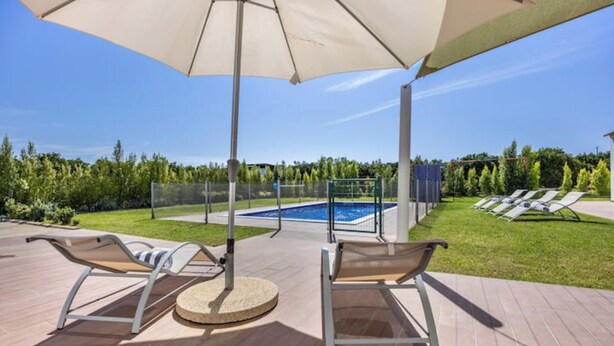 Zona de piscina amb gandules i una ombra, una piscina i vistes a la vegetació circumdant.