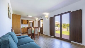 Un saló amb un sofà, taula de dinar amb cadires, armaris de fusta i una porta corredissa de vidre que dona a una zona exterior.