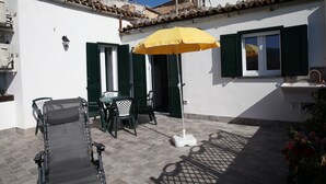 A patio with a table and chairs, a yellow umbrella, and a white wall with green shutters. - B&B Ex Albergo Centrale Atessa a place that has a history (Atessa)