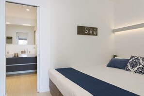 A bedroom with a bed, a bedside table, a wall-mounted light, and a bathroom visible through an open door.