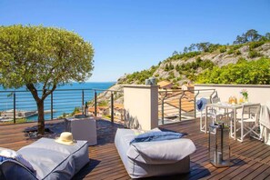 A wooden deck with outdoor seating, a table, and a view of the sea.