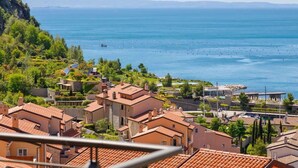 Un área residencial costera con casas de tejados de terracota, un puerto deportivo y una vista despejada del mar.