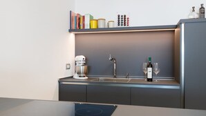 Una cocina moderna con horno empotrado, lavamanos y una botella de vino en la encimera.