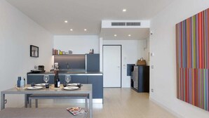 Una cocina moderna con comedor, una mesa pequeña con una revista y un cuadro abstracto de colores en la pared.