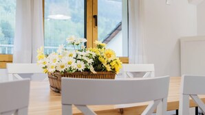 Ein Esstisch mit einer Blumenkorbdekoration, weißen Stühlen und einem Fenster mit Blick ins Grüne.