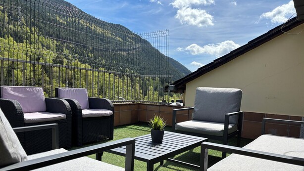 Eine Terrasse mit Korbmöbeln und einem kleinen Tisch, mit Blick auf eine Berglandschaft.