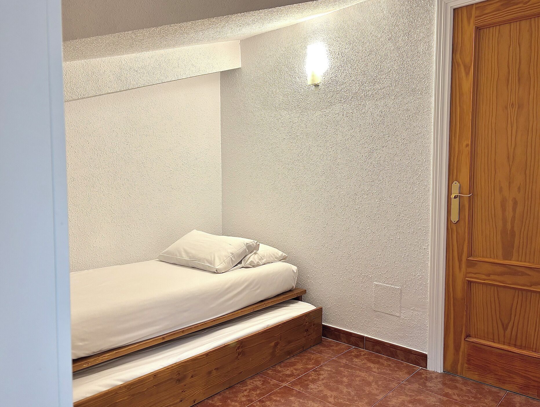 A small, compact bedroom with a bunk bed, a wooden door, and a textured wall.