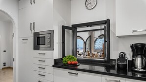 Une cuisine moderne avec des meubles blancs, un plan de travail noir, un four à micro-ondes, une machine à café et une horloge murale.