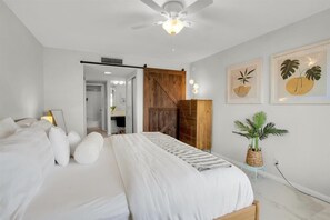 Une chambre à coucher avec un lit, un ventilateur de plafond, une porte en bois et des œuvres d’art encadrées accrochées au mur.
