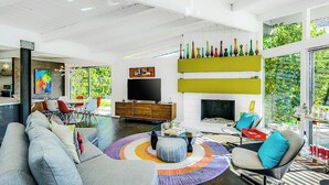Ein modernes Wohnzimmer mit Sofa, Couchtisch und Sesseln. Es gibt einen Flachbildfernseher, einen Kamin und einen Essbereich mit Tisch und Stühlen.