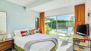 Ein Schlafzimmer mit Bett, Schreibtisch mit Fernseher und Blick auf Pool und Grünflächen.