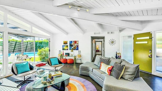 Ein modernes Wohnzimmer mit einem Glastisch, einem grauen Sofa und einem farbenfrohen Teppich.