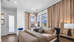 A bedroom with a bed, a nightstand, a chair, and a view of the outside. - The Desert Oasis Casita (Palm Desert)