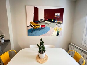 A dining area with a table, chairs, a potted plant, and a painting on the wall.