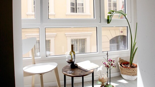 A room with a table, a chair, a potted plant, and a window with a view of buildings.