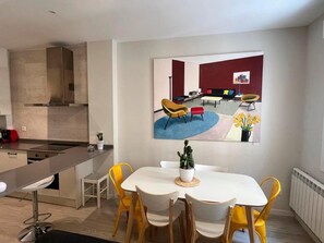 A modern kitchen with a dining area, a large window, and a painting of a living room.