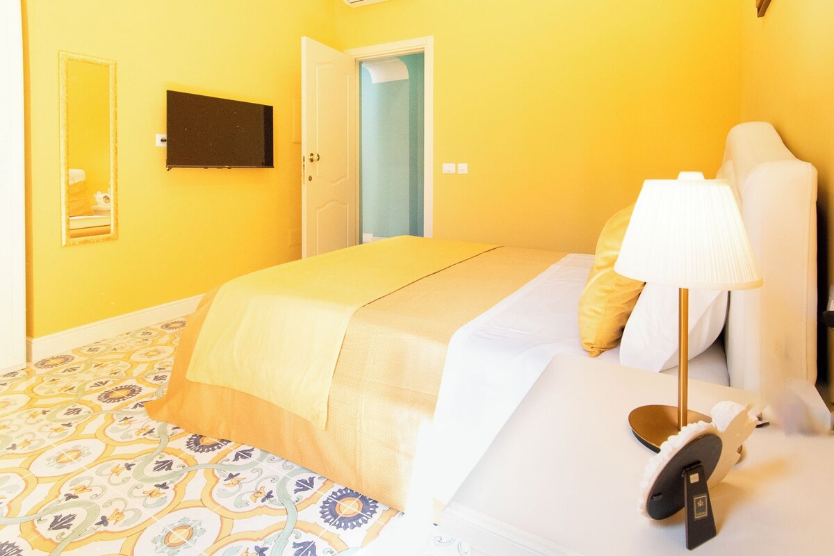 A hotel room with a bed, a bedside lamp, a door, and a mirror.