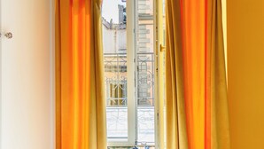 Ein Fenster mit orangefarbenen Vorhängen, einem Metallgeländer und Blick auf Gebäude.