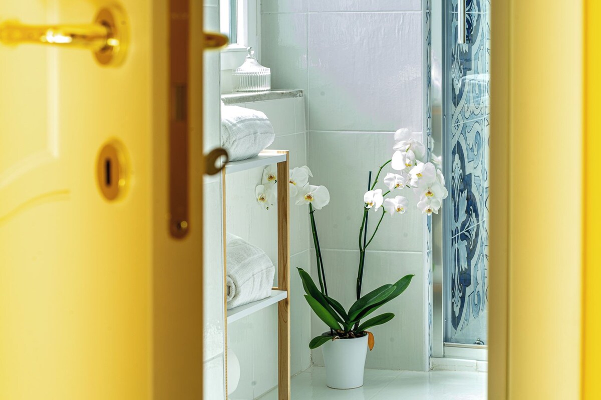 A bathroom with white tiled walls, a white sink, and a potted orchid plant.