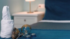 Ein ordentlich bezogenes Bett mit einer blauen Bettdecke, ein weißer Nachttisch mit einer Lampe und ein weißes Handtuch.