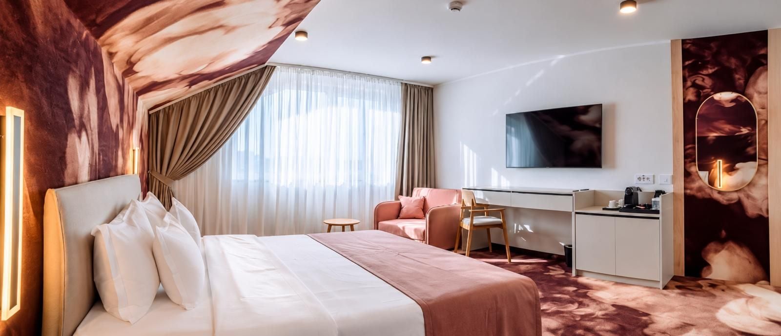 Habitación de hotel con cama, escritorio, silla, televisor y un espejo grande.