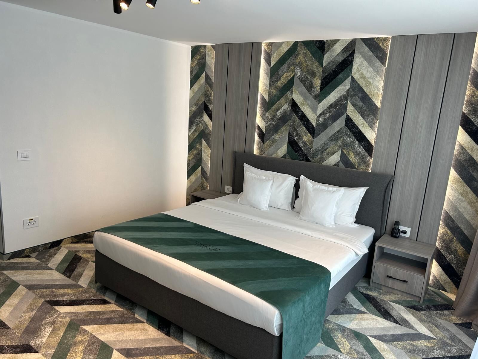 A modern hotel room with a large bed, a nightstand, and a patterned floor.