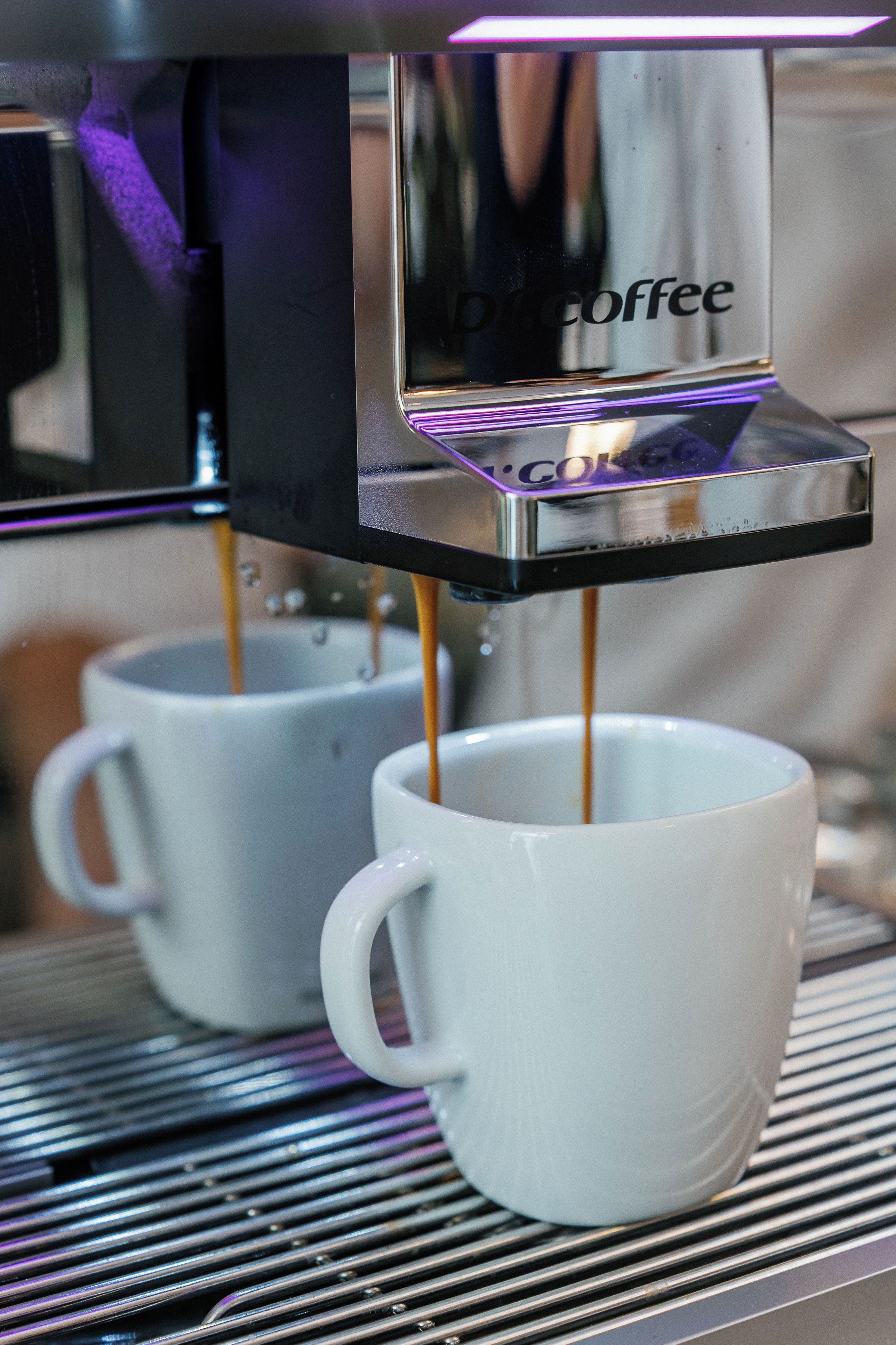 Een koffieapparaat schenkt koffie in twee witte kopjes.