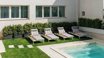A modern building with a swimming pool, multiple lounge chairs, and a well-maintained lawn.