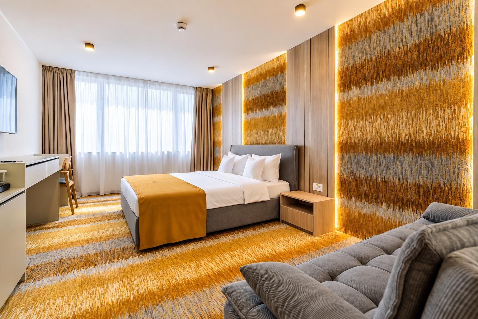 Quarto de hotel moderno com uma cama grande, um sofá, uma escrivaninha e uma parede com design texturizado.