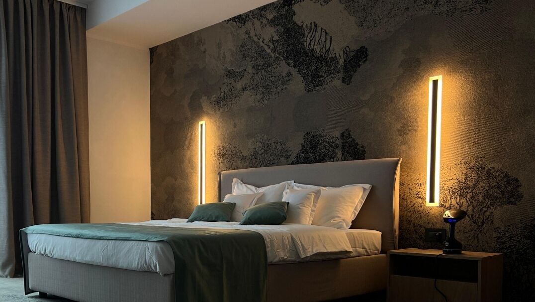 Een moderne slaapkamer met een groot bed, twee nachtkastjes en een wandlamp.
