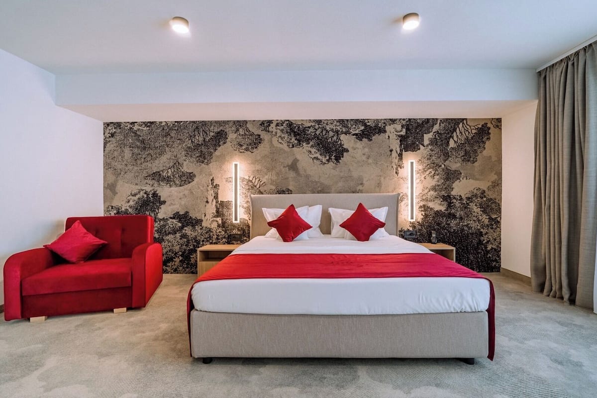 A hotel room with a large bed, a red armchair, and a textured wall.