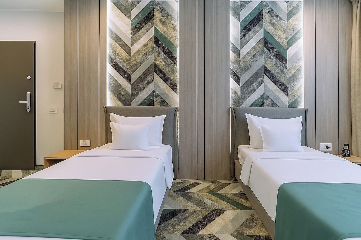 A hotel room with two beds, a wardrobe, and a chevron-patterned wall.
