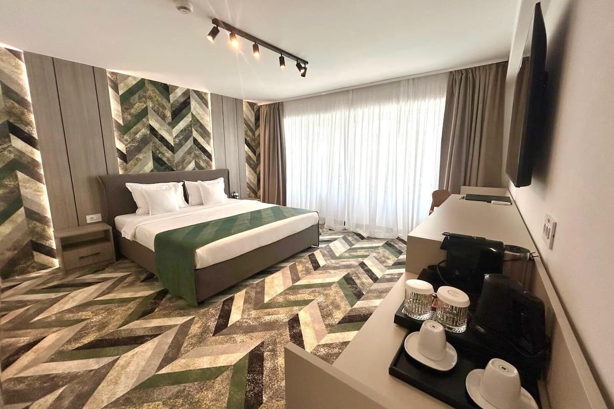 A hotel room with a bed, a desk with a coffee maker, and a TV.
