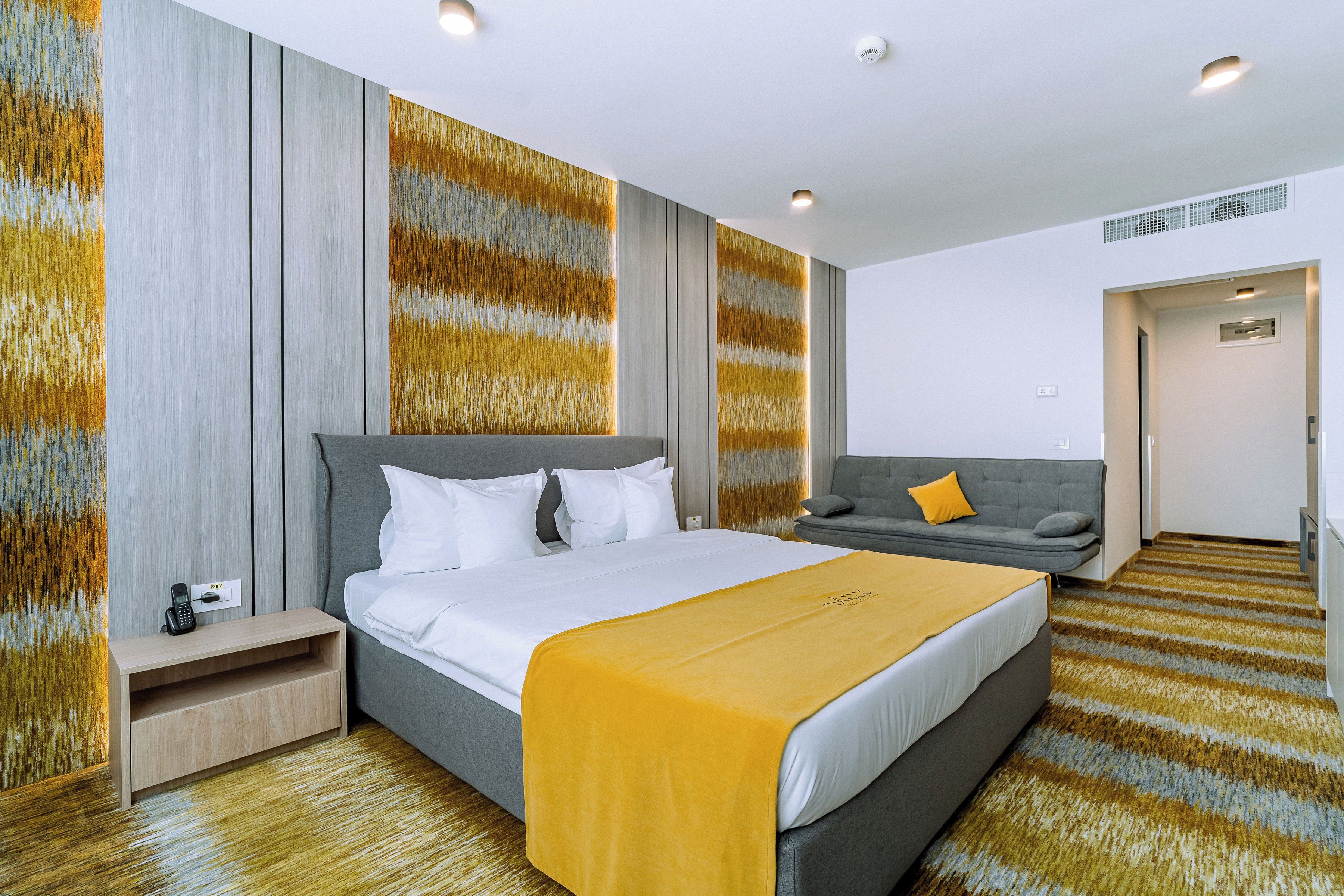 A modern hotel room with a large bed, a sofa, and a small desk.