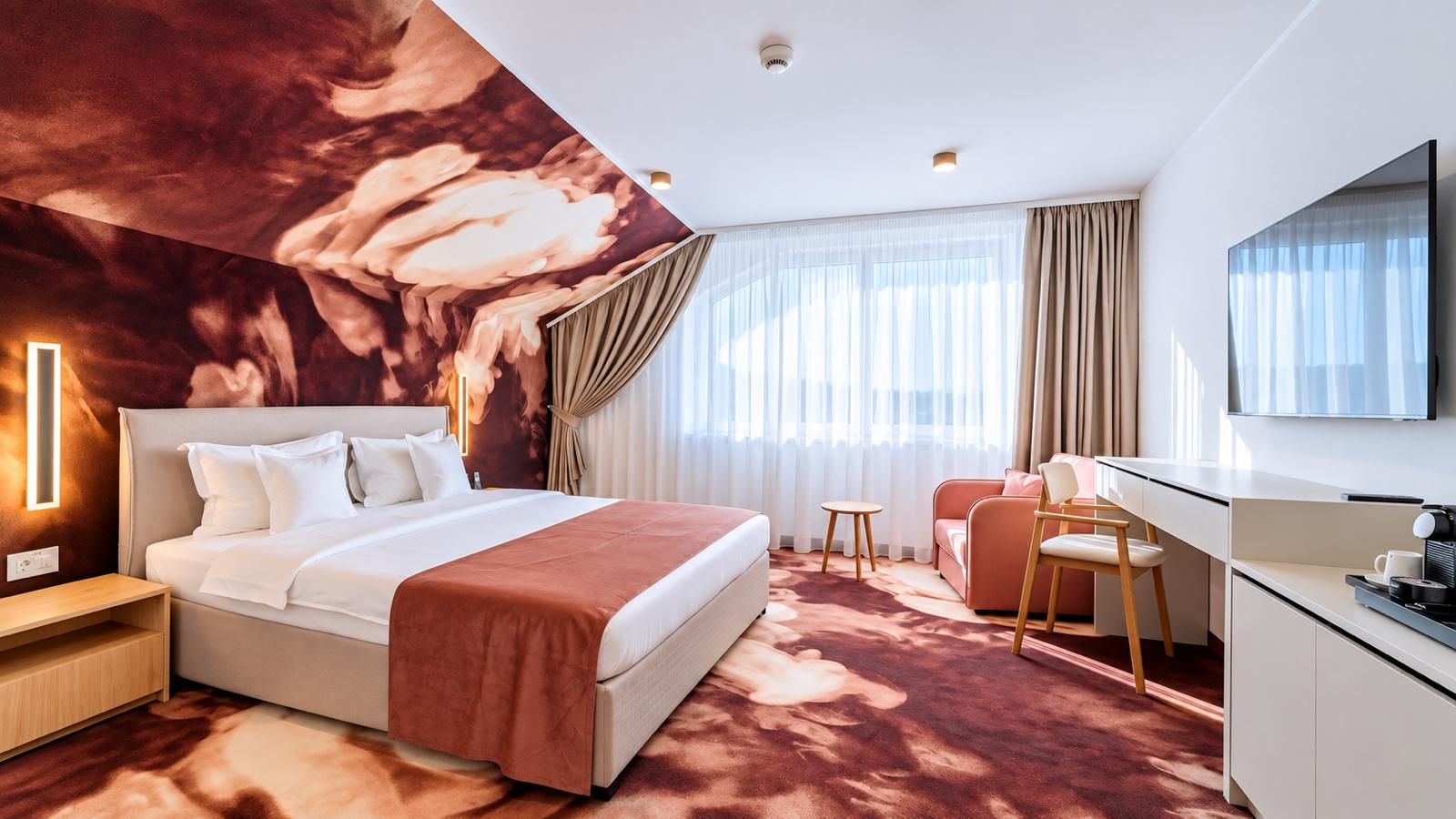 A hotel room with a large bed, a desk, a chair, a TV, and a ceiling mural.