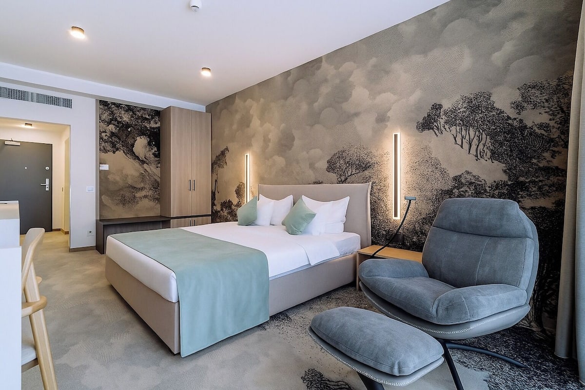 A modern bedroom with a bed, a chair, and a wall with a tree mural.