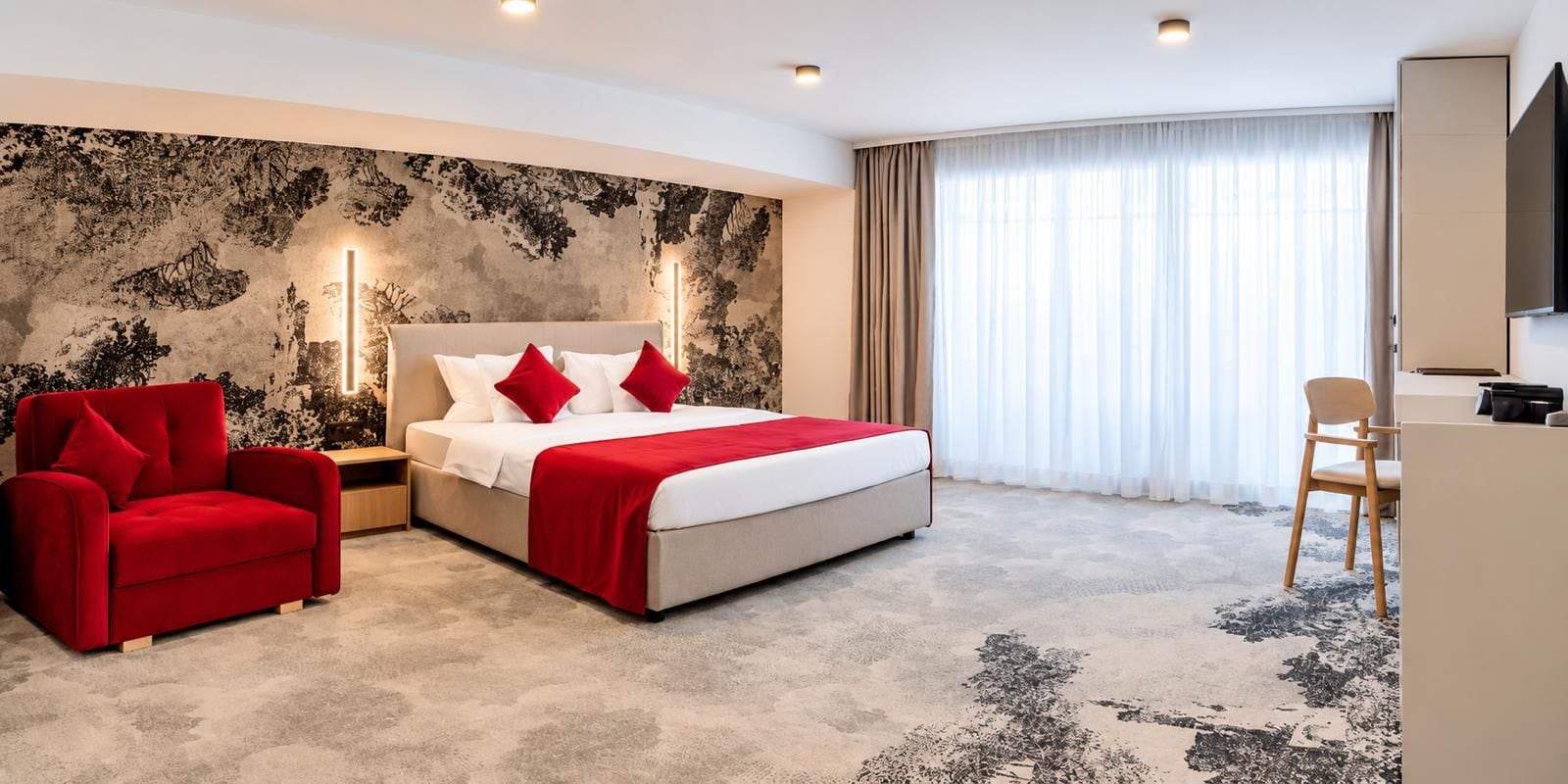 Een hotelkamer met een bed, een rode fauteuil, een bureau en een grote spiegel.