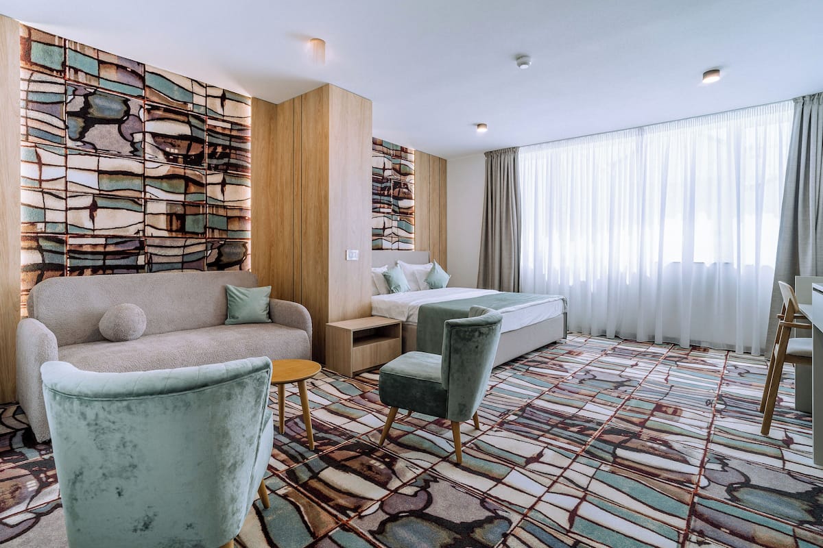 A hotel room with a sofa, a chair, a bed, a small table, and a decorative wall.
