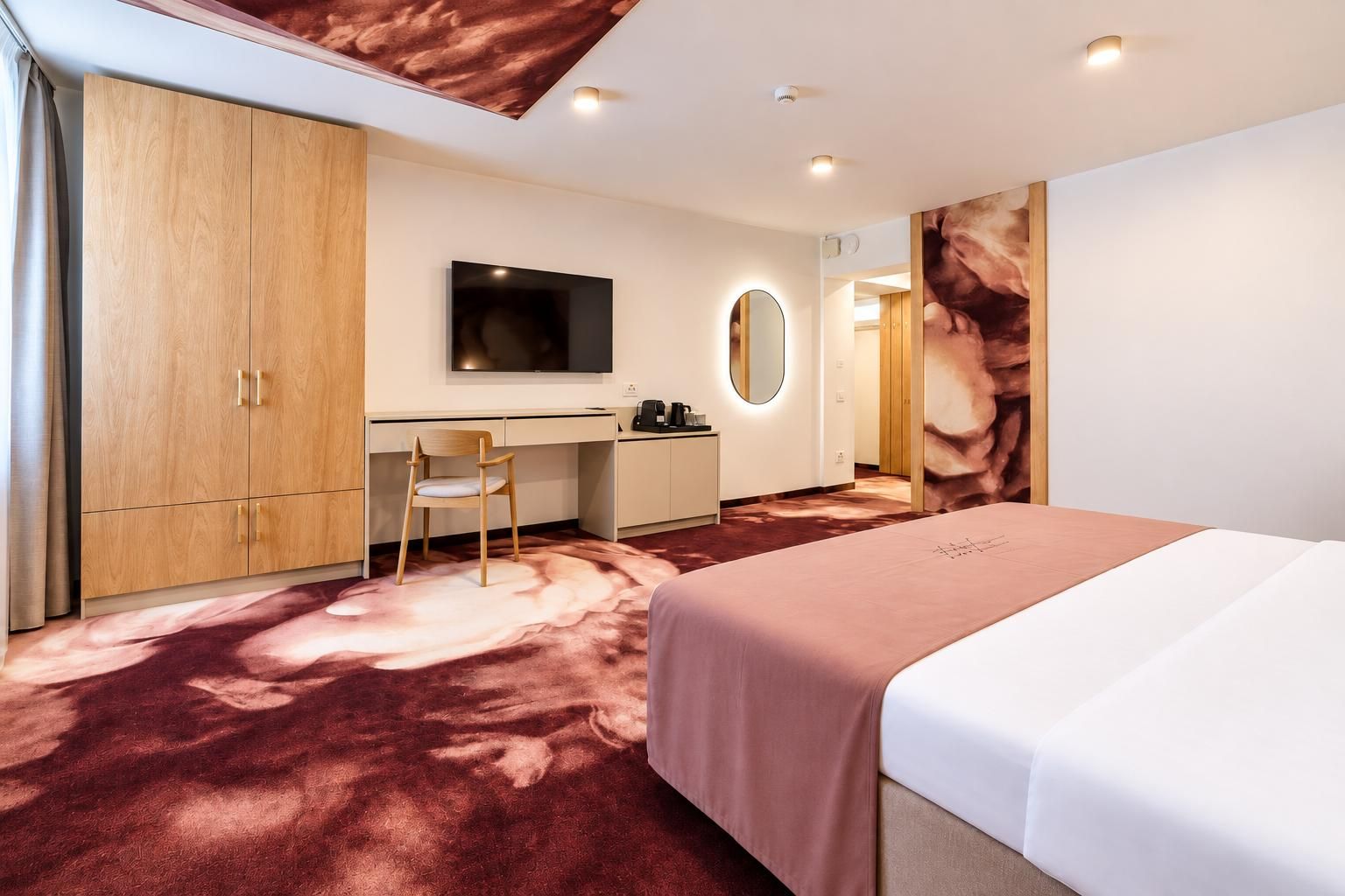 A modern hotel room with a bed, desk, chair, and a large mirror.