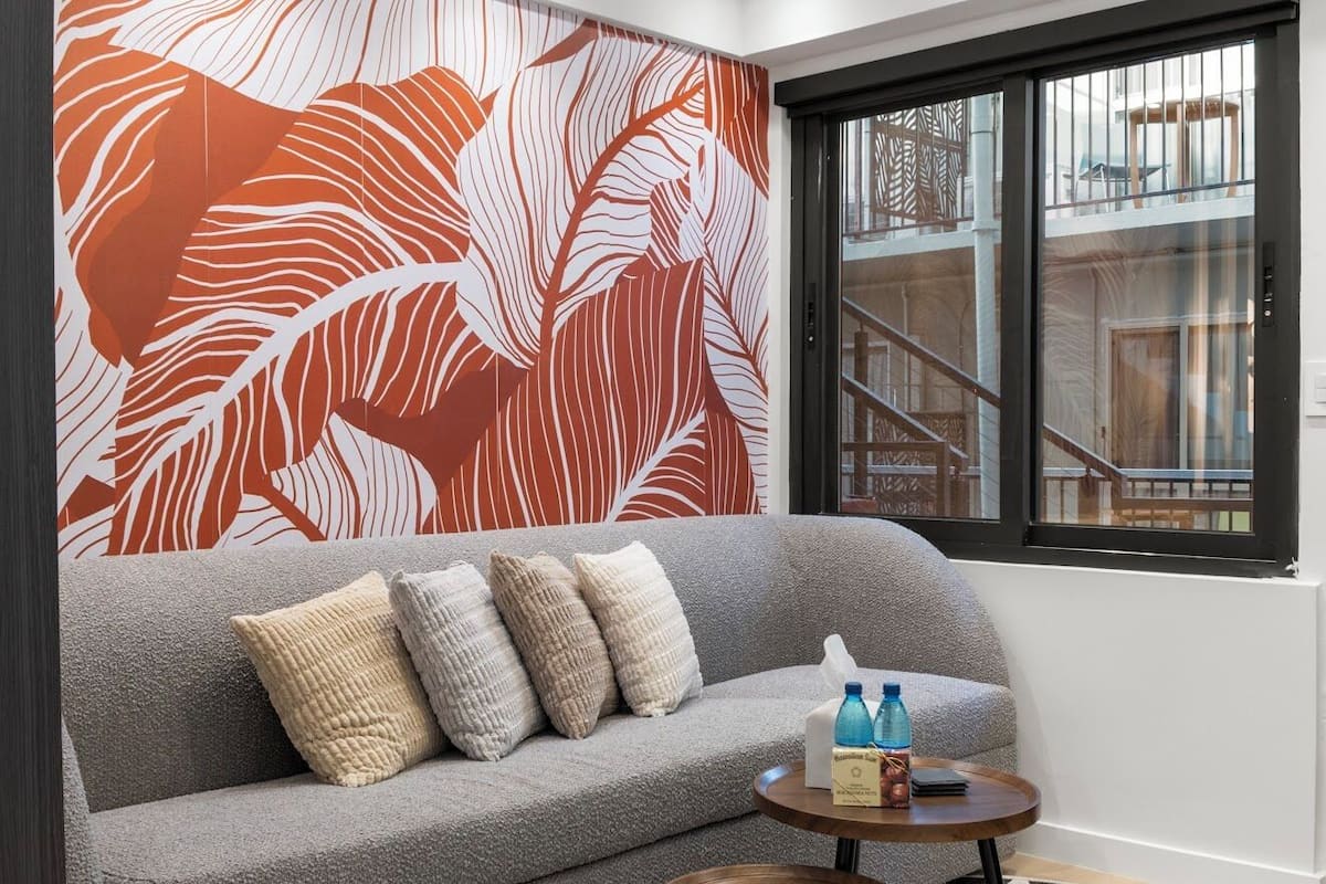 Un salon moderne avec un canapé gris, un mur à motifs et une fenêtre donnant sur une terrasse en bois et un escalier.
