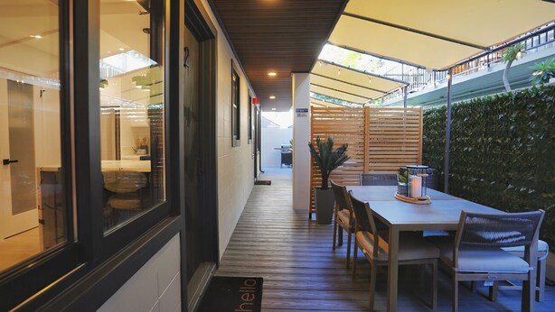 A modern outdoor dining area with a wooden table and chairs, a glass wall, and a wooden fence. - The Walk-Up Waikiki Beach  (Honolulu)