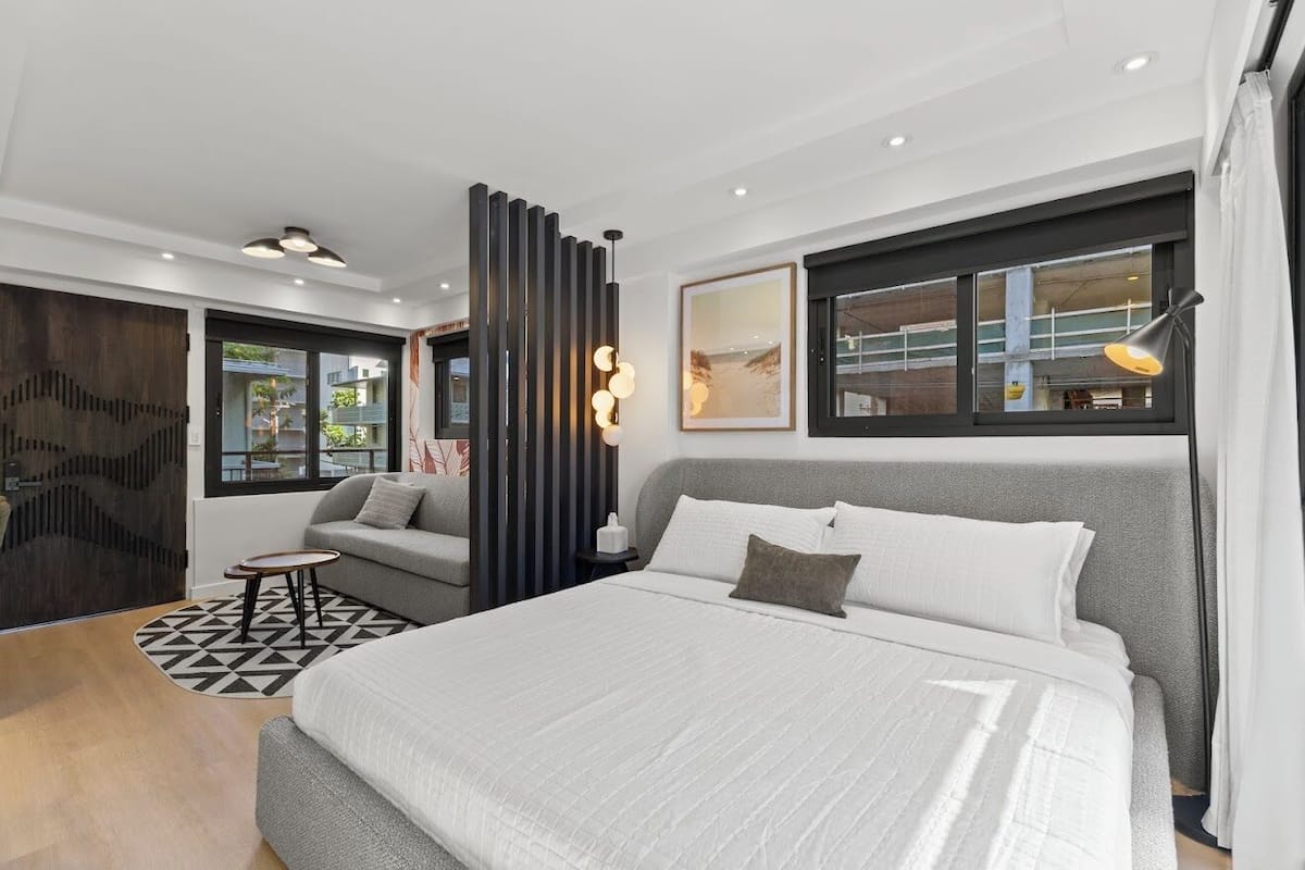 Une chambre d’hôtel moderne avec un grand lit, un canapé, une petite table et un panneau décoratif mural.